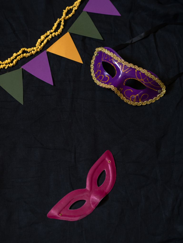Purple and pink masquerade masks with decorative banners on a dark fabric backdrop.